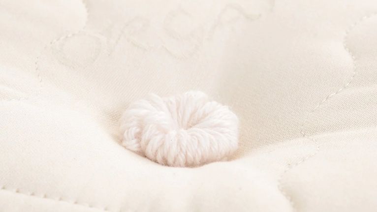 Close-up of a hand-tufted detail on a cream-colored mattress