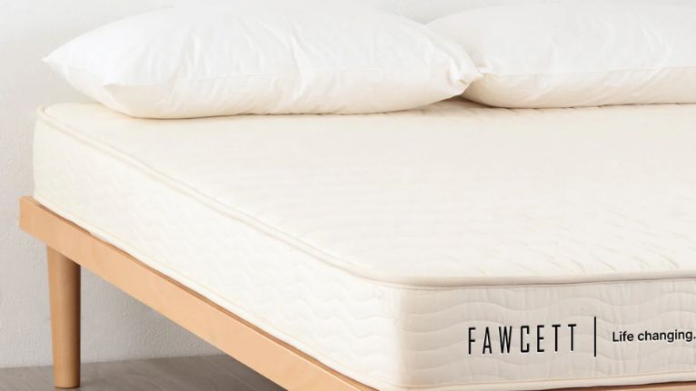 close-up of a mattress on a light wooden bed frame with two pillows