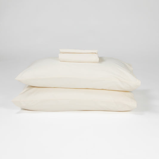 Fawcett Organic Cotton Bed Sheet Set stacked with pillows natural