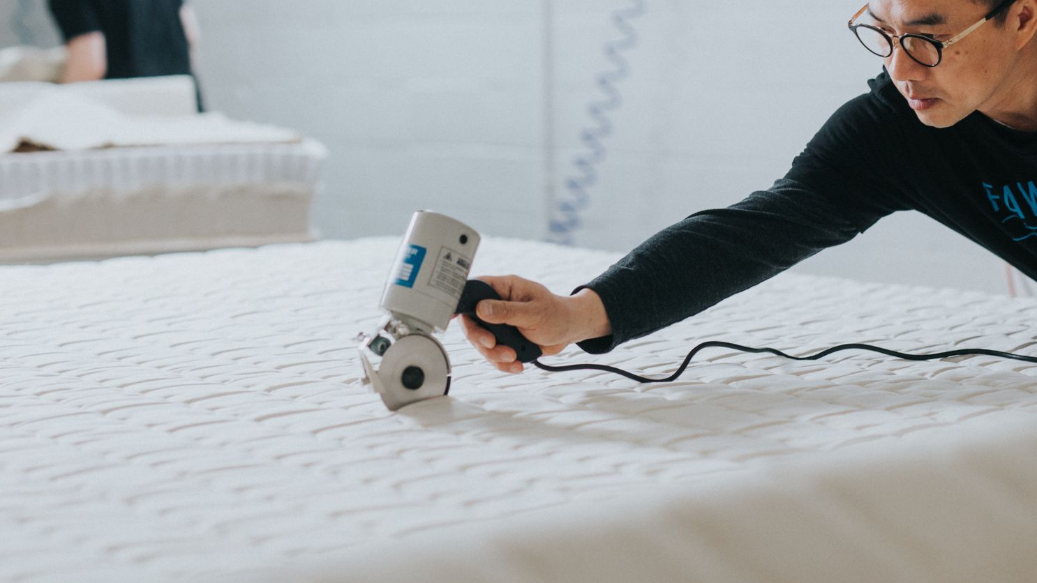 Person inspecting and cutting mattress fabric.